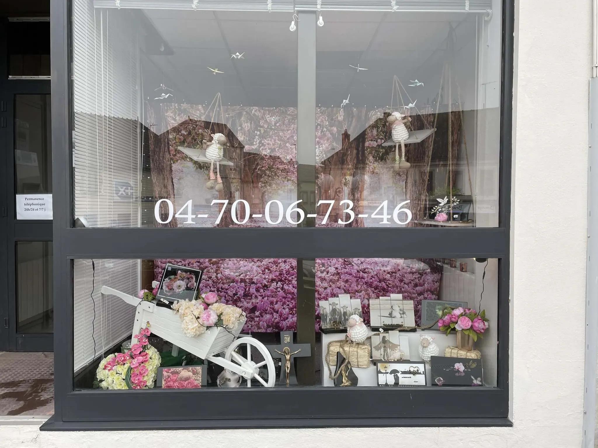 Vitrine des Pompes Funèbres Lamarque avec composition florale, brouette blanche et numéro de contact