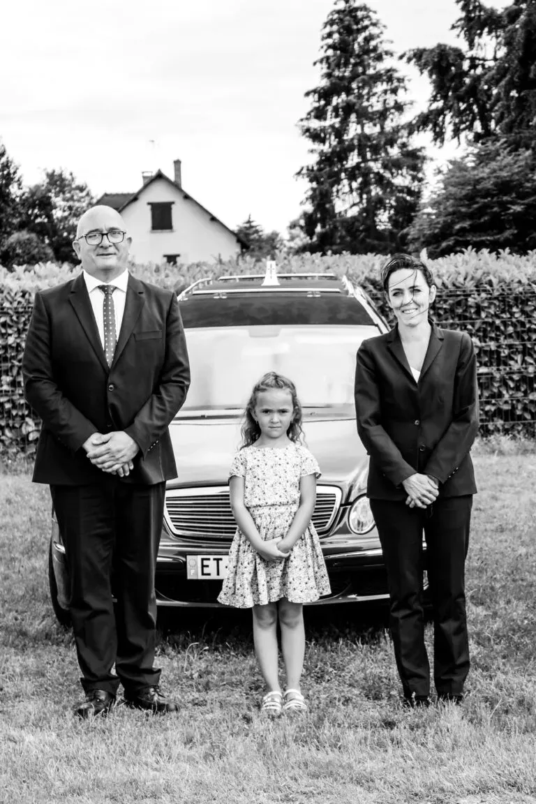 Portrait de famille en noir et blanc des Pompes Funèbres Lamarque devant un corbillard Mercedes