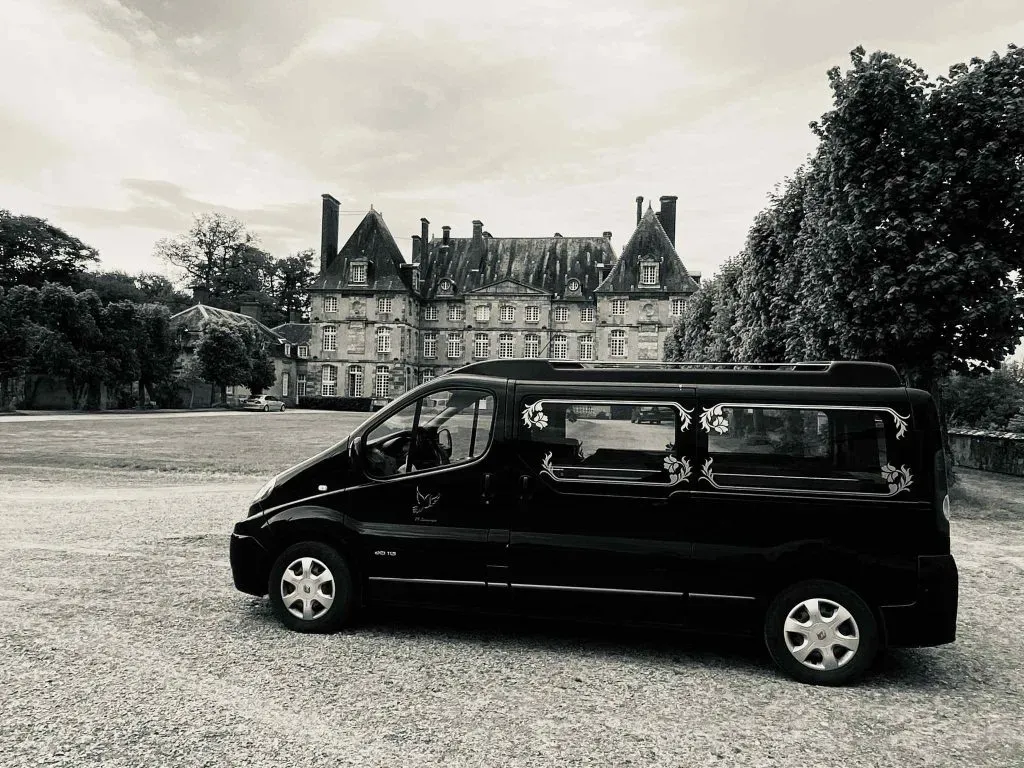 Corbillard noir stationné devant un grand château ancien photographié en noir et blanc