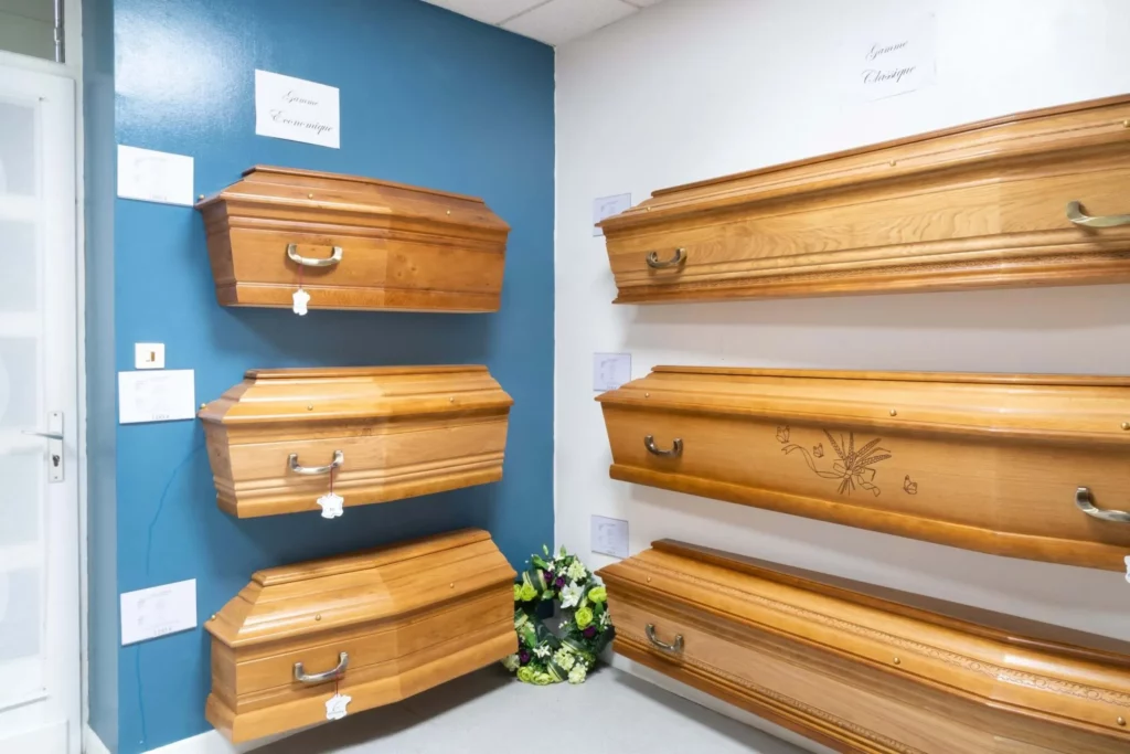 Exposition de cerceuils en bois dans une salle de présentation aux murs bleu et blanc